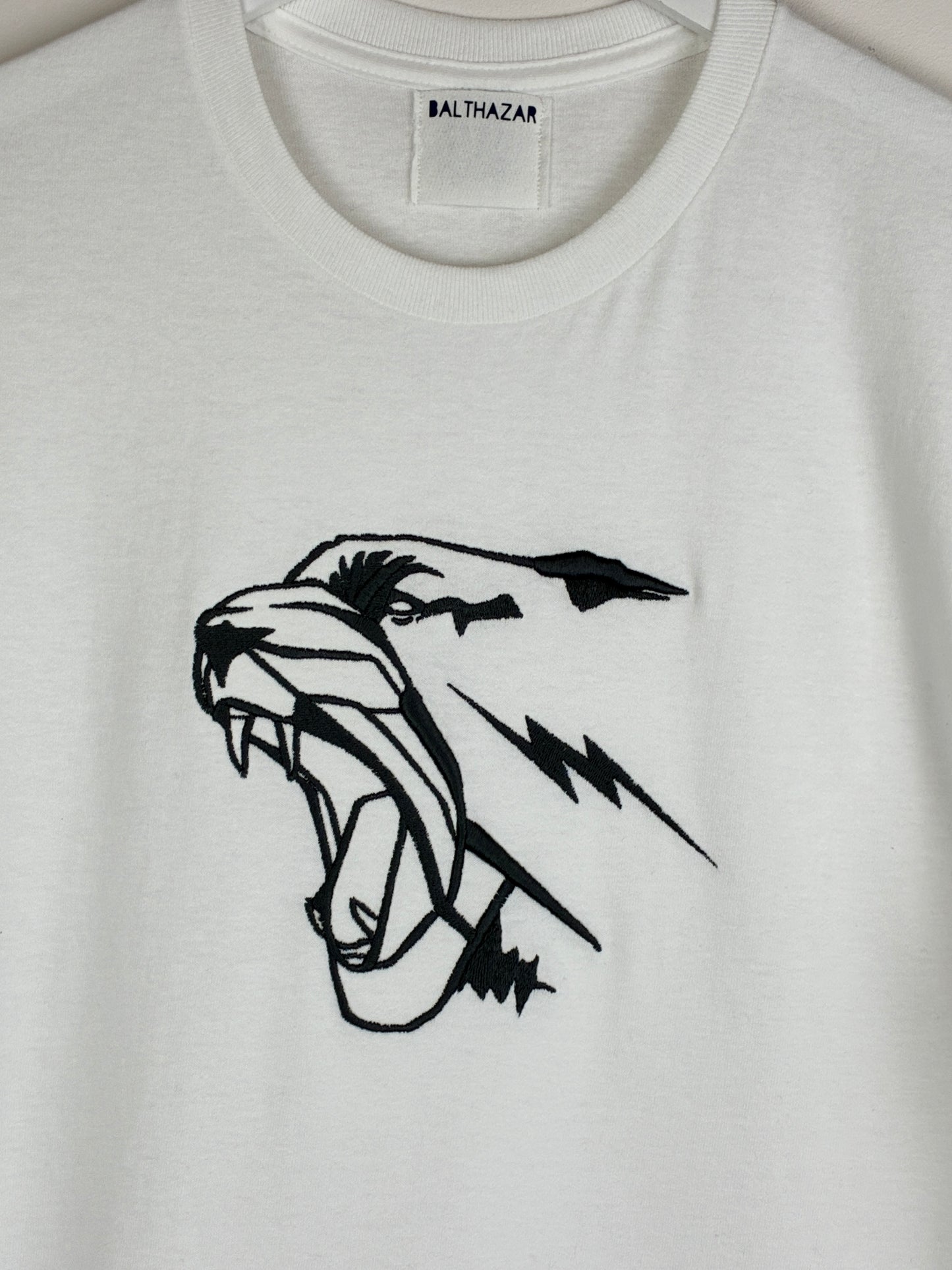 White t-shirt with an embroidered graphic style leopard head, measuring 7 inches in width by 6.5 inches in width and positioned in the centre of the chest. Statement style design that is customisable with your choice of embroidery thread.
