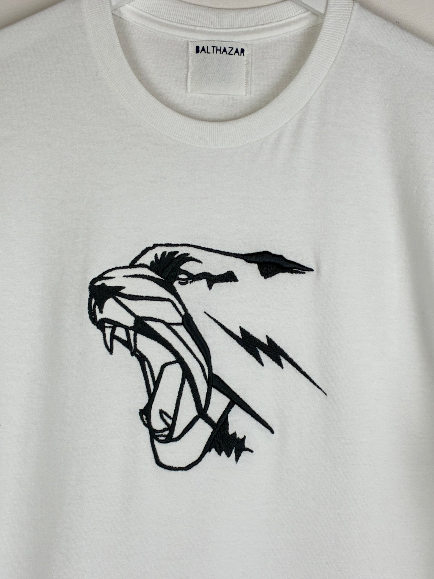 White t-shirt with an embroidered graphic style leopard head, measuring 7 inches in width by 6.5 inches in width and positioned in the centre of the chest. Statement style design that is customisable with your choice of embroidery thread.